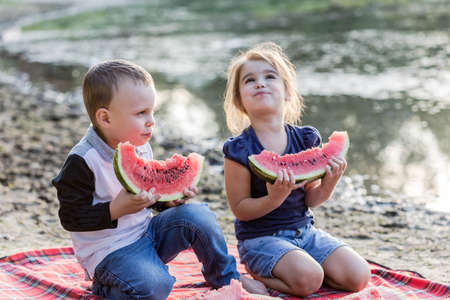 Family and friends summer vacation. Happy kids eating watermelon and sit on the beach over sunset.の写真素材