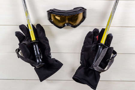 Overhead view of ski accessories placed on rustic white wooden table. Items included goggle, gloves and ski sticks. Winter sport leisure time concept.の写真素材