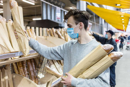 Young man wearing disposable medical mask shopping in supermarket during coronavirus pneumonia outbreak. Protection and prevent measures while epidemic time. Covid-19 personの写真素材