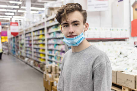 Young man wearing disposable medical mask shopping in supermarket during coronavirus pneumonia outbreak. Protection and prevent measures while epidemic time. Covid-19 personの写真素材