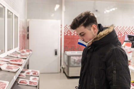 Young man wearing disposable medical mask shopping in supermarket during coronavirus pneumonia...