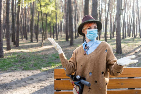 A stylish woman wearing mask and gloves to defened her from coronavirus. Using electric scooter in city and park to be in safe.の写真素材