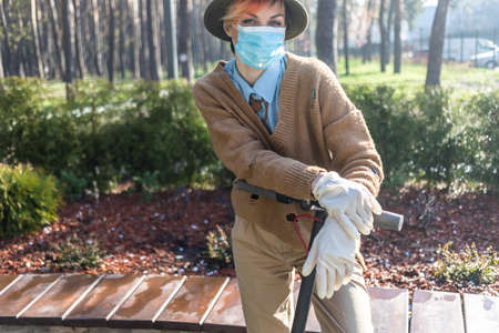 A stylish woman wearing mask and gloves to defened her from coronavirus. Using electric scooter in city and park to be in safe.の写真素材