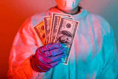 Doctor in protective wear holding money. Vaccine from, flu, coronavirus, ebola.の写真素材