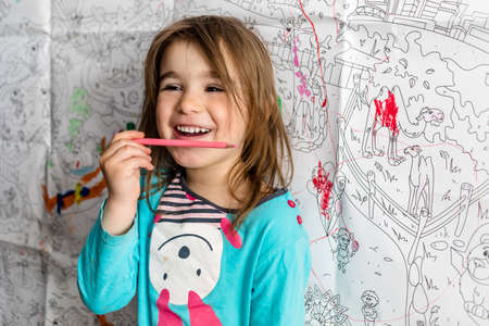 Covid-19 Coronavirus and Learning from home.  Cute little girl coloring on her wall at home....