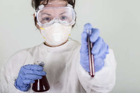 Doctor in protective wear holding test tube with blood for Coronavirus COVID-19 analyzing. Vaccine...