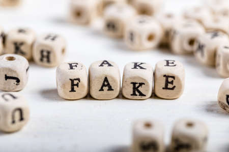 Word FAKE formed by wood alphabet blocks. On old wooden table.の写真素材