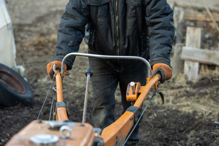 Man farmer working in field ploughing the land with a plough on a farm. Ploughman on a walk behind motor cultivator. Season processing soil in village. Organic cultivate natural products. Agricultureの写真素材