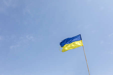 Damaged Ukrainian flag over blue sky during war with russia.の写真素材