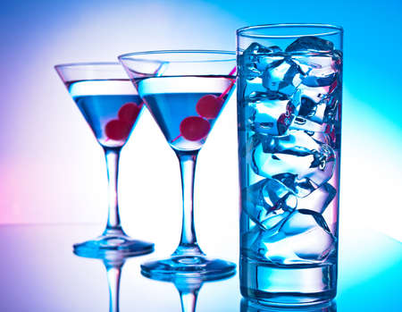 Two glasses of martini with red cherries and a glass of clear cocktailの写真素材
