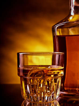 Glass and a bottle of whisky against red and yellow backgroundの写真素材
