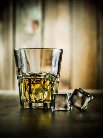 Glass of whiskey on the rocks on a wooden background