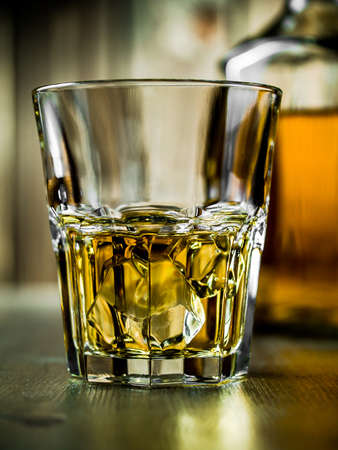 Glass of whiskey on the rocks and a bottle on a wooden backgroundの写真素材