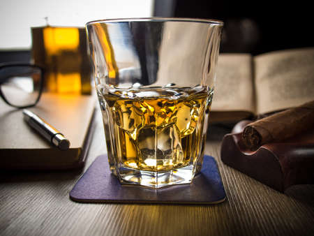 Glass of whiskey on a table with books, cigar and spectaclesの写真素材