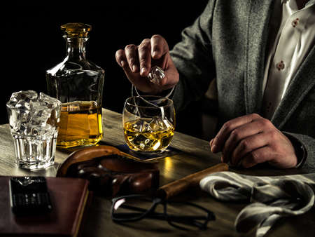 Businessman relieving stress after a hard working day drinking whiskey and puts an ice cube in his glassの写真素材