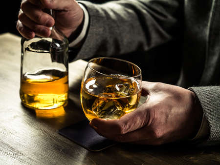 Man wearing jacket holding a glass of whiskey at the bar counterの写真素材