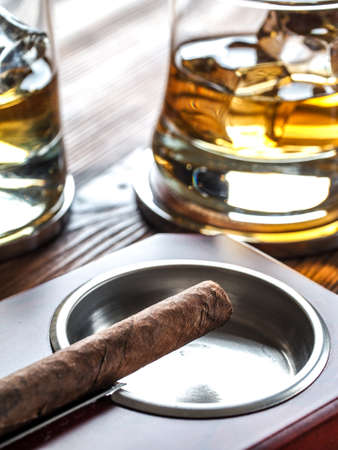 Glass of whisky on the rocks and a cigar in an ashtray