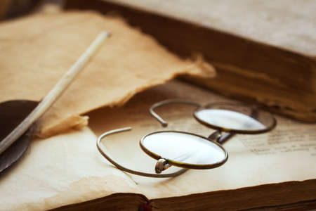 vintage spectacles with quill pen and piece of paper on bookの写真素材