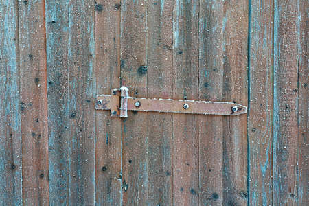 Rusty locking slide latch on frozen wooden old door in the winter with snow flakes on it as a rustic...