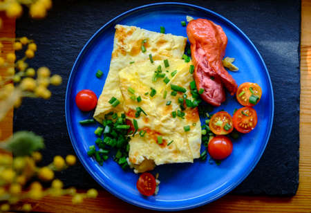 Omelette with tomatoes, green onion on blue plateの写真素材