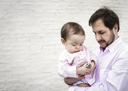 Father holding baby boy son at a blank white brick wall