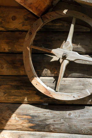 Old wooden wheel suspended on a rustic wooden wall, half in shadow, half illuminated by the sunの写真素材