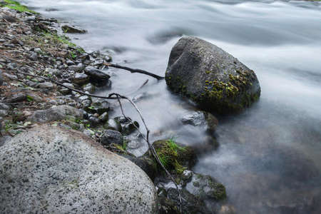 Water, photographed at a slower shutter speed, wraps around the stones that are in the riverの写真素材