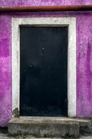 Black metal closed door on a stone wall of purple colorの写真素材