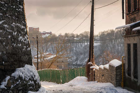 Bending streets of the old city. Snow-covered town with a green old fence, historic buildings aroundの写真素材