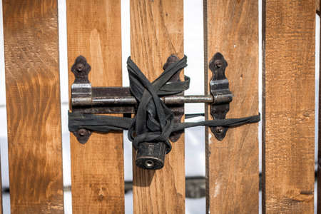 Old black padlock on a wooden yellow fenceの写真素材
