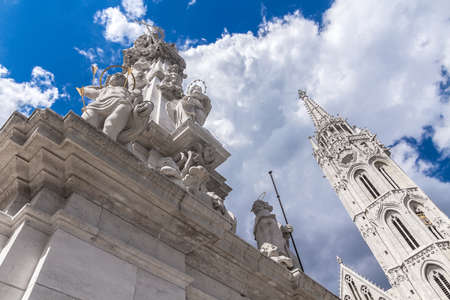 Close-up of plague pillar on the background of the Cathedral of St. Matthias in Hungary, in Budapest. White sculpture with gold elements under the blue skyの写真素材