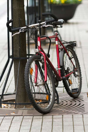 Red city bike parked next to a tree on the lock in the city of Vilnius, Lithuaniaの写真素材