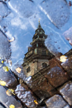 Tower of Catholic Duomo in the center of Riga, Latvia is reflected in a puddle in the fall, among fallen leaves and paversの写真素材