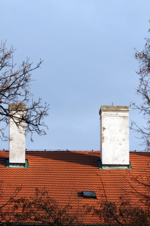 Two chimneys on red tiled roof on one of the historic buildings in the center of Prague on the background of bright blue skyの写真素材