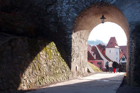 Large group of people passes through the arch, which is overgrown with moss. Against the background of the arch is a famous city of Cesky Krumlovのeditorial素材