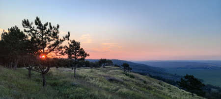 Sunset on the mountain. The light of the setting sun extends to the mountain and the valley of endless fields below. The crimson sky will shine to the horizonの写真素材