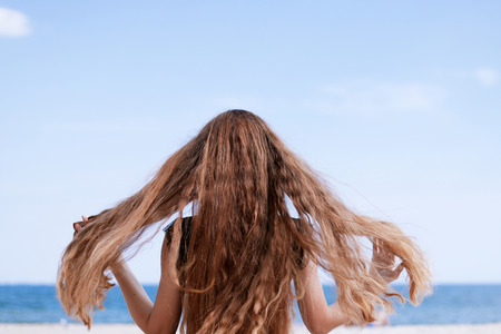 girl with long brown hair sitting on the beachの写真素材