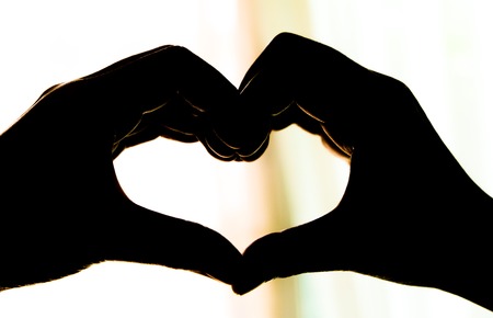 Creative silhouette heart shape from hands against with sunlight.