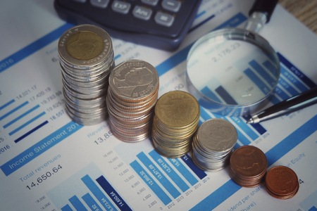 Coins stacking and chart with magnifying glass for analyzing financial report of value investor in stock market concept.の写真素材