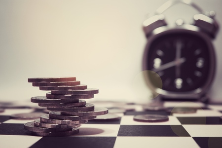 Money coins stack on chess table with alarm clock and white background. This photo for financial and...