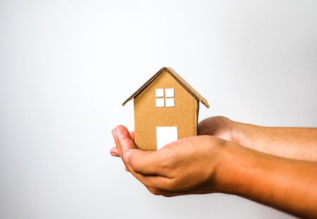 Brown house model in 2 human hands on white background. House investment and debt concept.の写真素材