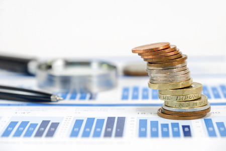 Close up pound sterling coins stacking on capital graph with pen and magnifier glass for investment concept.の写真素材