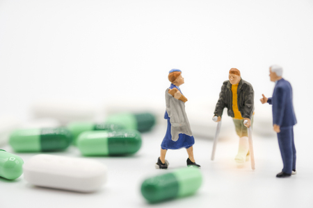 Miniature of old man broken legs nurse and hospital manager around with Pharmaceutical medicine pills, capsules and tablets on white background. Hospital concept - Imageの写真素材