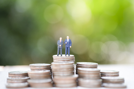 Miniature figure business man manager standing on glowing coins stack with greenery background. Successful investor concept.の写真素材