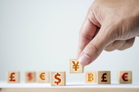 Hand putting China Yuan sign to US dollar sign on wooden cube. It is symbol of economic tariffs trade war and tax barrier between United States of America and China.の写真素材
