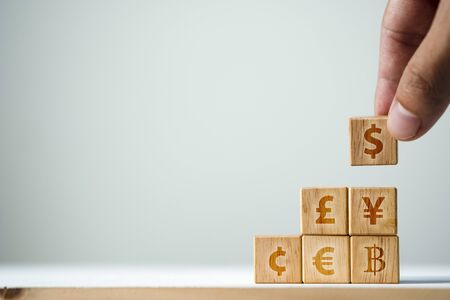 Hand putting wooden cube of US dollar sign to Yuan  Yen Euro and Pound sterling sign. US dollar is main and popular currency of exchange in the world.Investment and saving concept.の写真素材