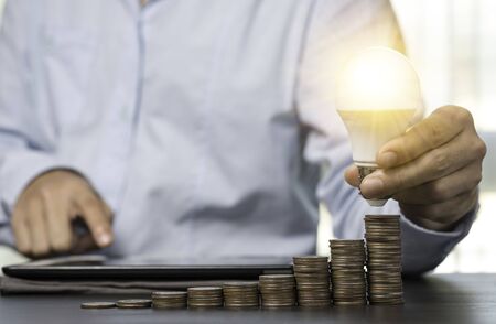 Businessman holding lightbulb which glowing on coins stacked. Creativity idea can make more money...