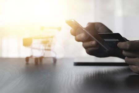 One hand holding credit card and another hand input order to mobile phone with shopping cart...