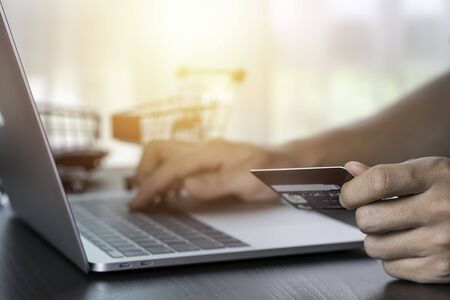 One hand holding credit card and another hand input order to computer laptop with shopping card...
