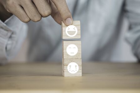 Customer hand putting happy  and smile face emotion which print screen on wooden block on sad emotion face. Customer service evaluation and copy space concept.の写真素材